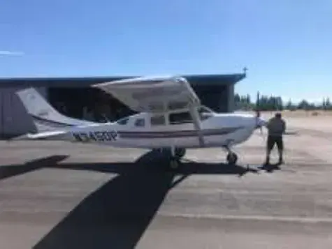 A man standing beside a white high-wing Cessna on the ramp