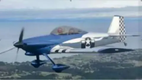 A blue and white RV homebuilt airplane in flight over water