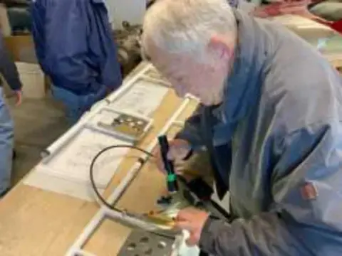 An older man working on a wing part at a workbench