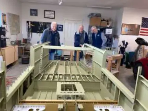 A fuselage frame on stands in a busy workshop