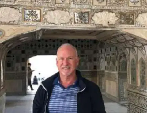 A smiling man standing in an ornate stone archway