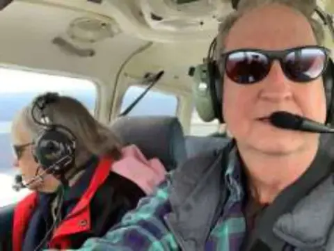 A man in sunglasses and a headset taking a selfie with a passenger