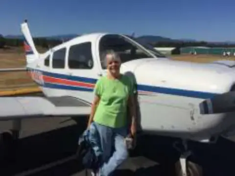 A woman standing beside a red, white and blue low-wing airplane