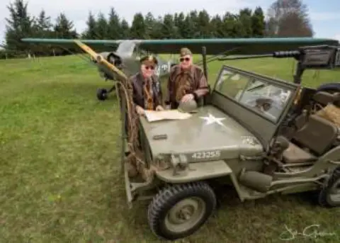 Men in period uniforms beside a vintage military jeep