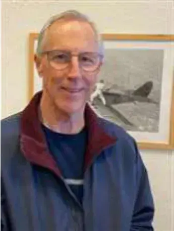 A smiling man in front of a framed airplane drawing