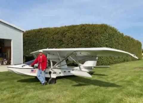 A man standing beside a white amphibious airplane outside a hangar