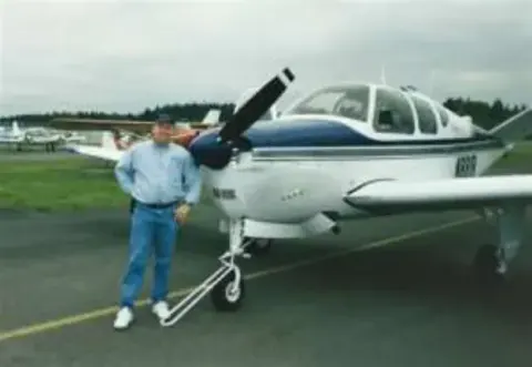 A man walking beside a white and blue low-wing airplane