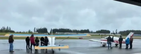 A group of people standing on the ramp near small airplanes