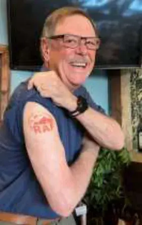 A smiling man showing a bandage on his upper arm