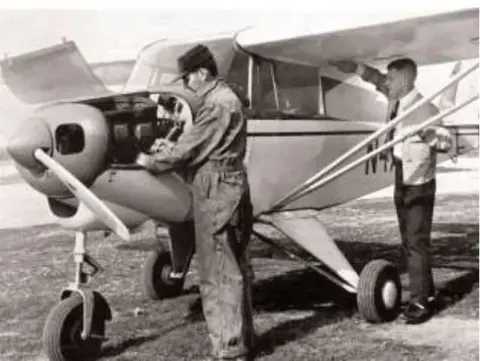 An old photo of two men next to a high-wing airplane