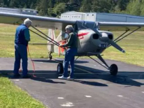 Two men pushing a high-wing taildragger on the ramp
