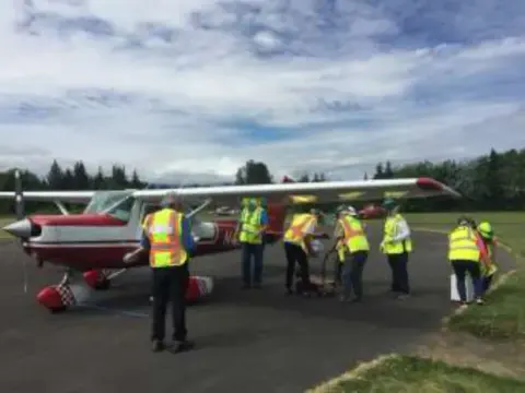 Volunteers in high-visibility vests gathered around a red and white Cessna on the ramp at Sequim Valley Airport