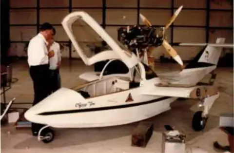 A man standing beside a white amphibious airplane in a hangar