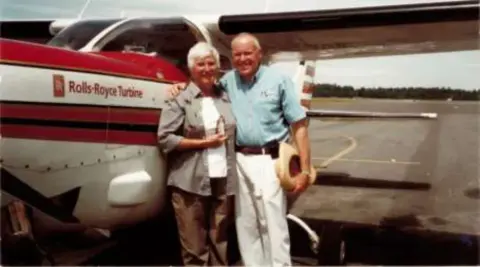 An older couple in front of a red and white airplane