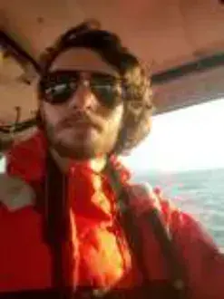 A young man in sunglasses and an orange jacket taking a selfie in a cockpit