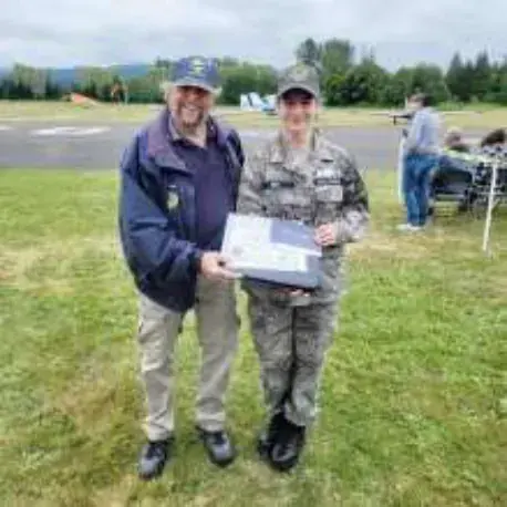 A pilot and a young flyer holding a certificate on the grass