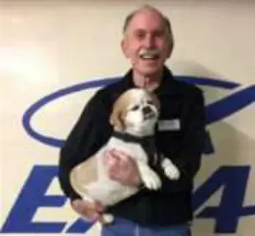 A smiling man holding a small dog in front of an EAA logo