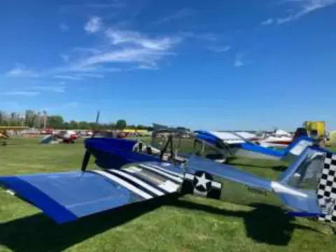 A blue and white homebuilt airplane parked among others on the grass at AirVenture