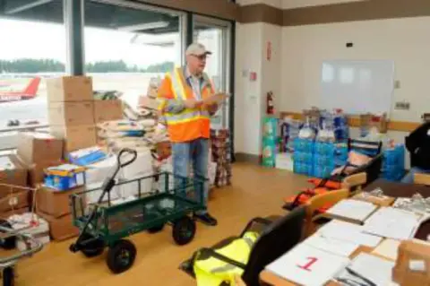 A volunteer in a safety vest pushing a cart of supplies in a warehouse