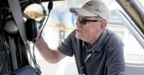 An older man in a cap leaning into an airplane door