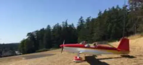 A red and white airplane parked on a grass strip by the trees