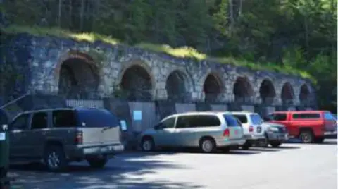 Cars parked in front of a stone wall with arches