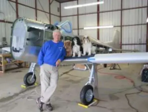 A man standing beside a silver vintage airplane in a hangar