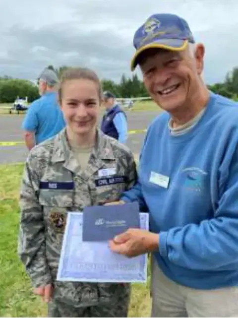 A young cadet holding a certificate beside an older pilot