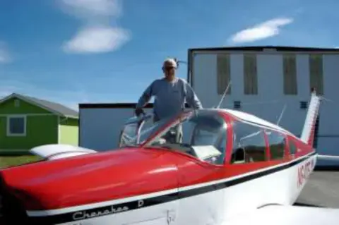 A man climbing into a red and white low-wing airplane