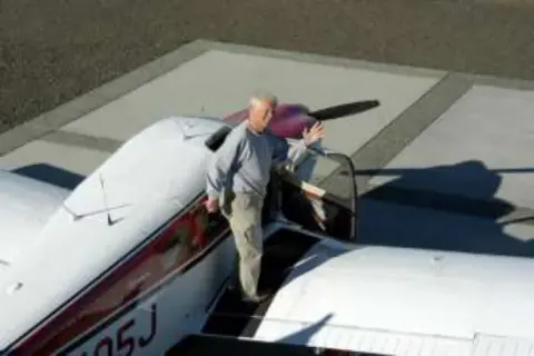 A man stepping onto the wing of a white low-wing airplane