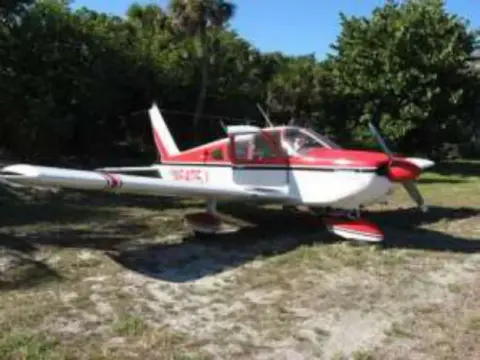 A red and white low-wing airplane parked near palm trees