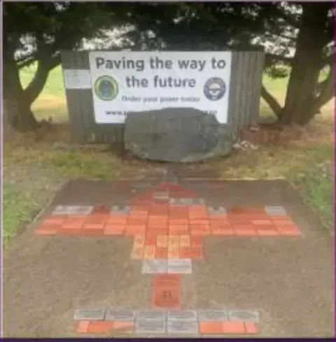 The brick patio laid in the shape of an airplane beside the Paving the Way sign