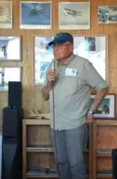 A man speaking into a microphone in front of framed pictures
