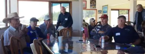 Members seated at tables in a room with large windows