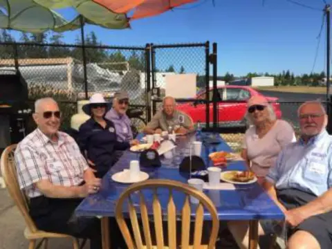 Members eating lunch at an outdoor table under an umbrella
