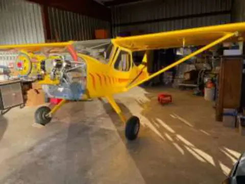 A yellow high-wing airplane with its cowling off in a hangar