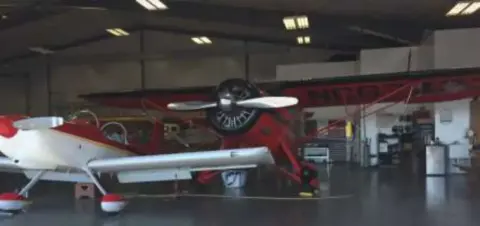 A red and white aerobatic biplane in a hangar