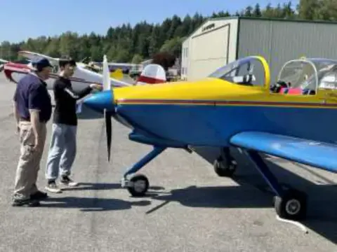 Two people beside a blue and yellow low-wing airplane on the ramp
