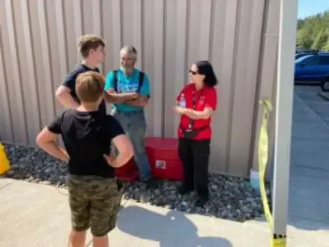 A boy and two adults talking beside a hangar