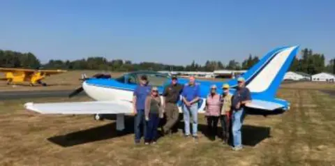 Members standing beside a blue and white low-wing airplane