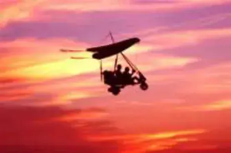 A powered parachute silhouetted against a sunset