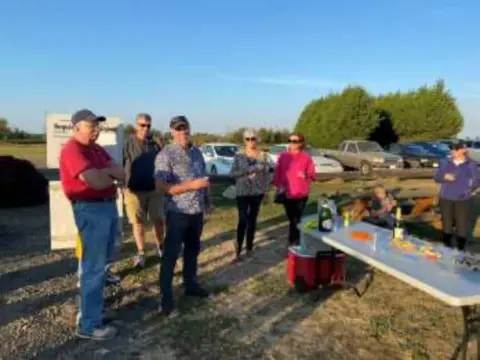 Members gathered at an outdoor table on the airfield at sunrise