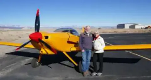 A couple standing by a yellow homebuilt airplane on the ramp