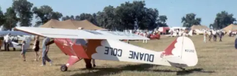 A red and white high-wing airplane at a fly-in