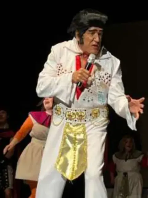 An Elvis impersonator performing in a white jumpsuit