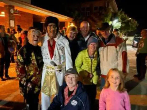 A crowd posing with an Elvis impersonator at night