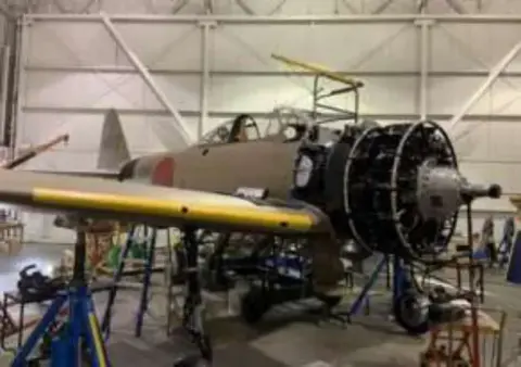 The A6M3 Zero under restoration in a hangar, its engine uncovered