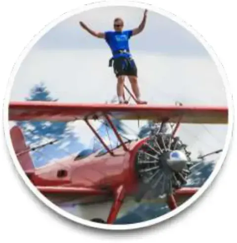 A wing walker standing on top of a red biplane