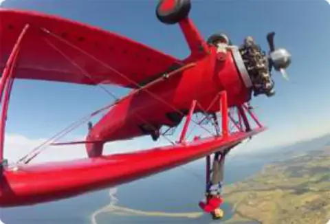 A red biplane in a steep bank over the countryside