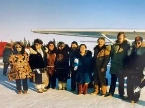 A group of people bundled up for cold weather in front of an airplane